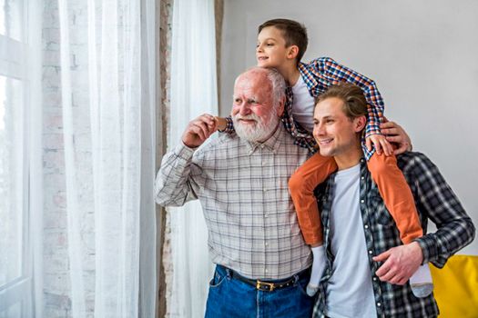 Anciano junto a hijo y nieto dentro en su casa mirando por la ventana