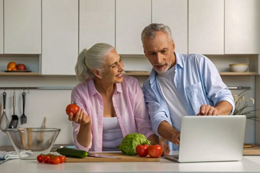 Pareja de adultos mayores mirando una laptop en la cocina